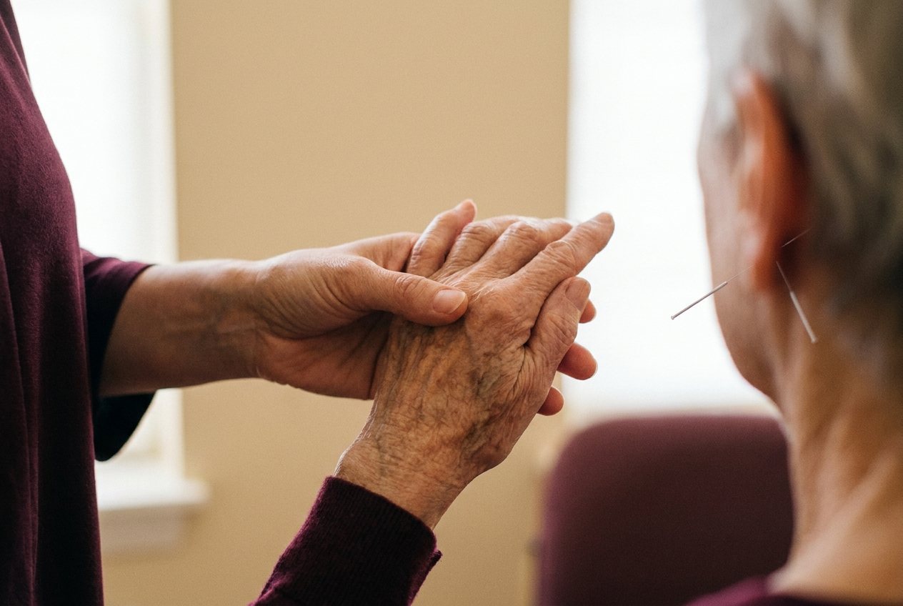 Cadrage serré sur deux mains : une praticienne accompagne le geste de la main ridée d'un patient âgé